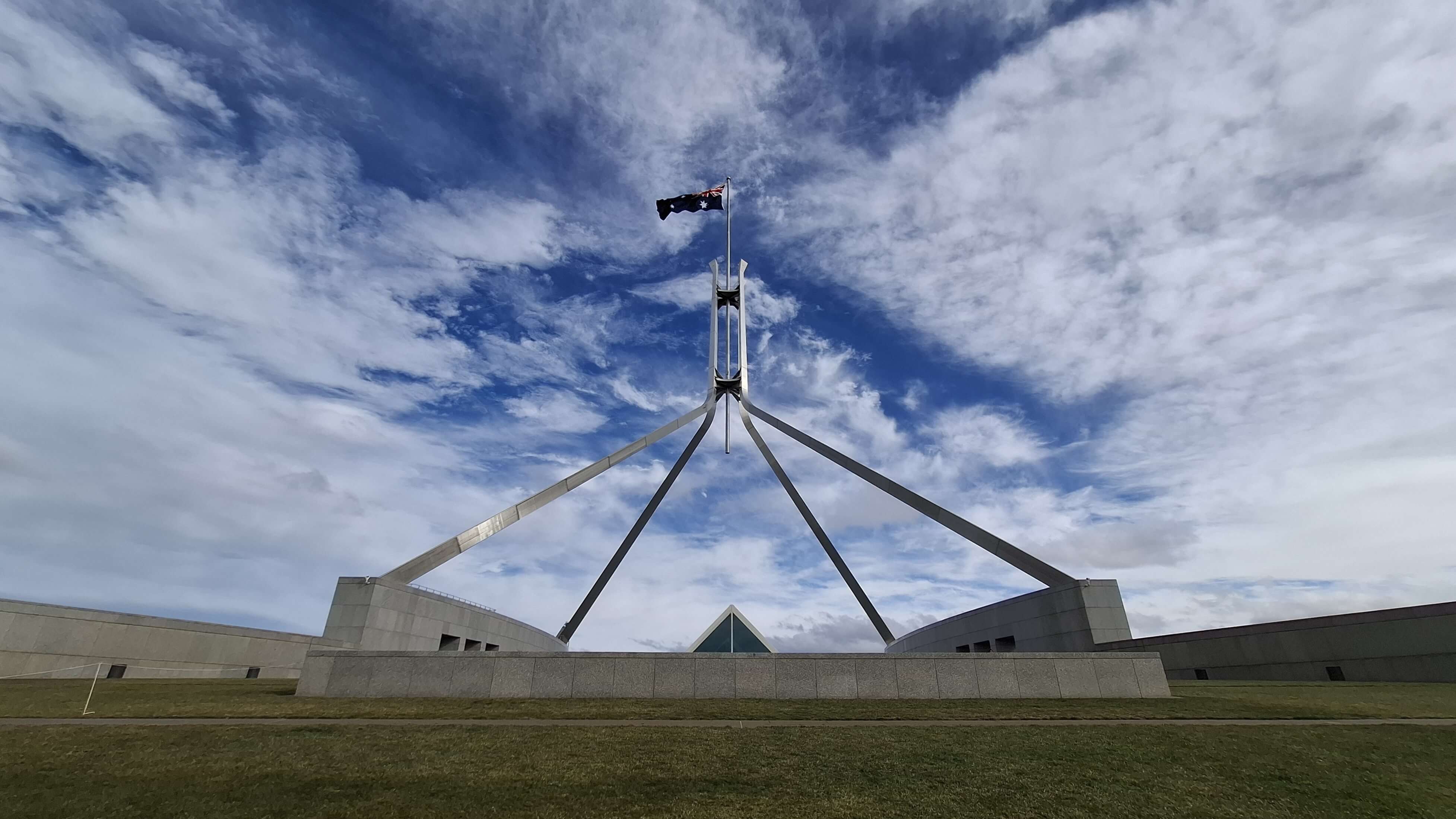 The flag of Australia, atop a large flagpole pyramid, against a blue sky.